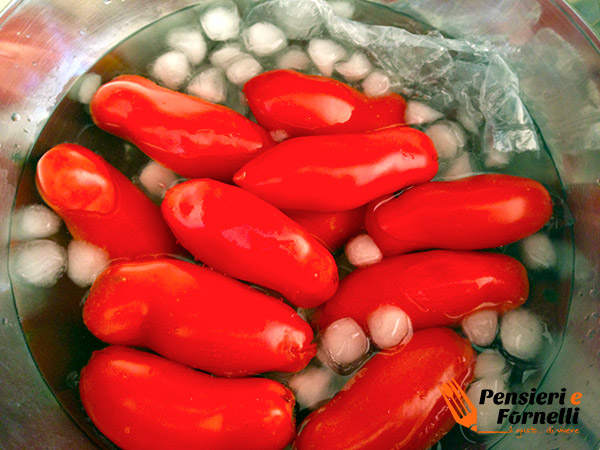 I pomodori sono immersi in una ciotola con acqua e ghiaccio per facilitare la pelatura